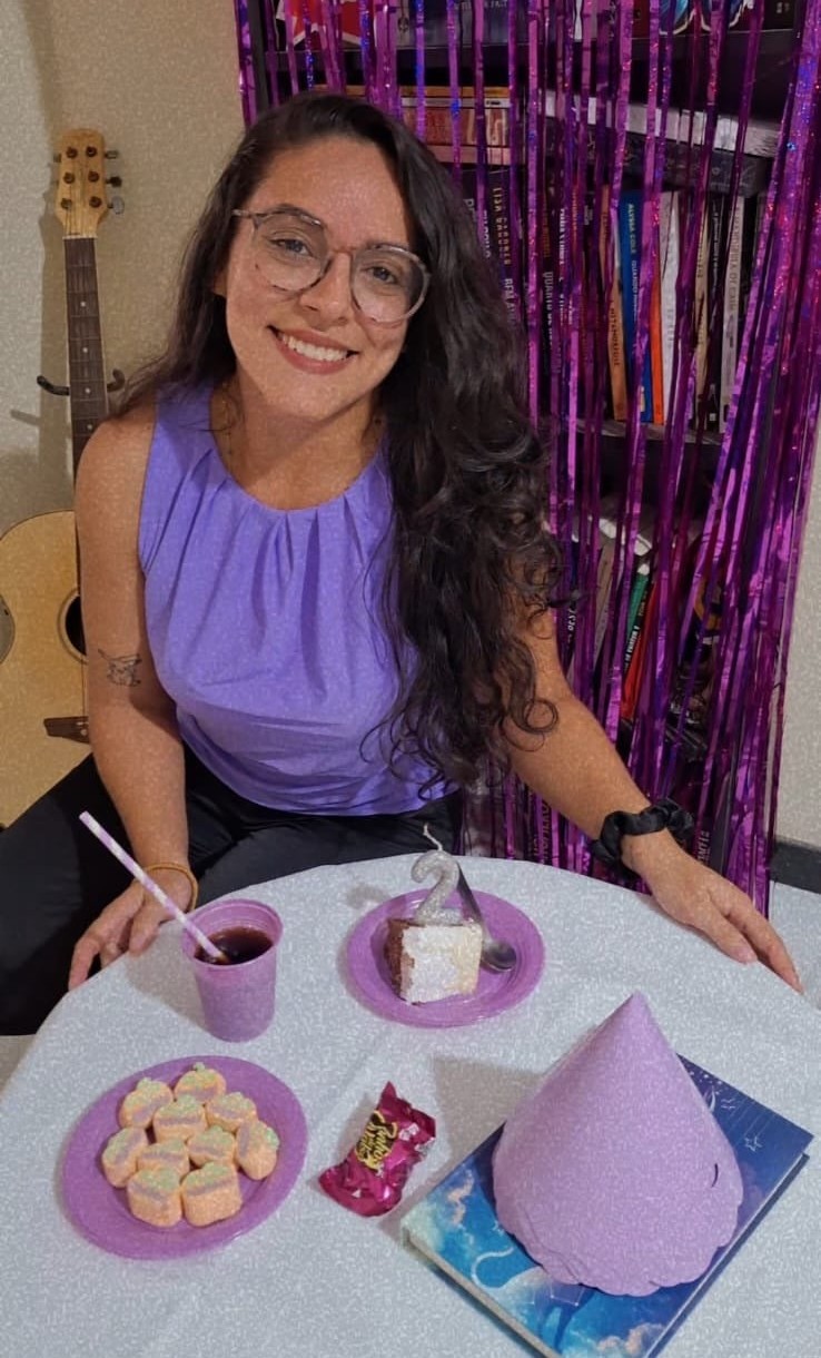 Mayara Trevizani sorrindo diante de sua estante de livros
